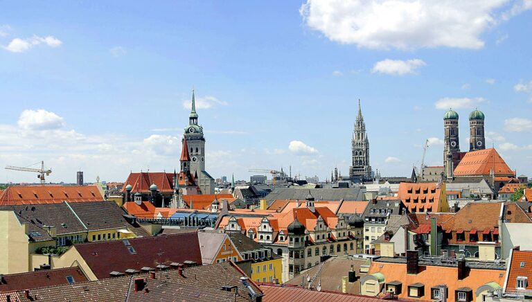 Aerial view of a European city with colorful buildings and prominent church spires under a blue sky.