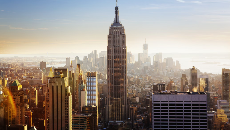 The iconic Empire State Building stands tall amid the New York City skyline bathed in golden sunset light.