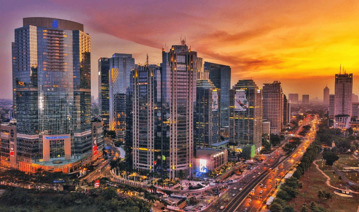 A vibrant cityscape at sunset with illuminated skyscrapers and a busy street.